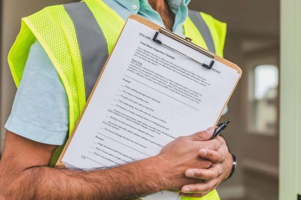 the torso and arm of a home inspector in a safety vest holding a clipboard of home inspection paperwork